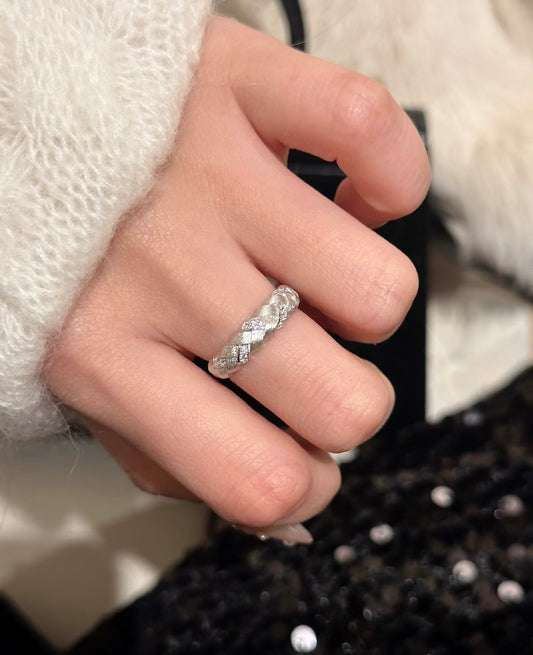 Hand wearing a silver ring with a textured band against a blurred background