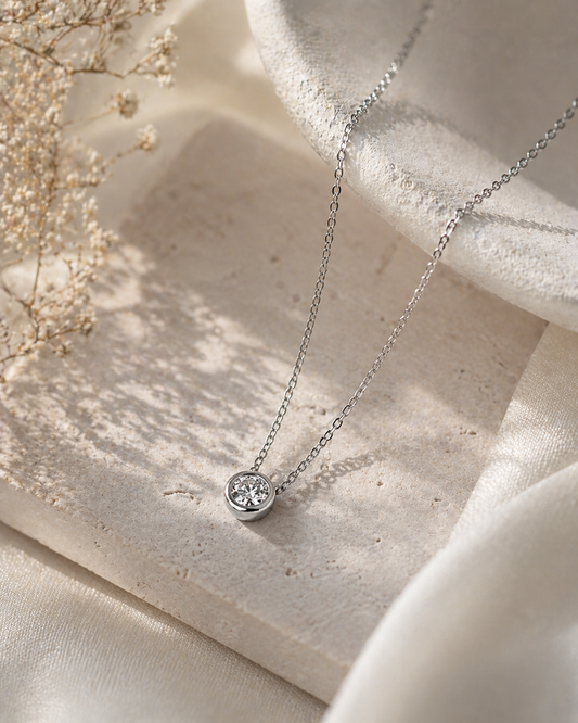 Silver necklace with a small round pendant on a light wooden surface.