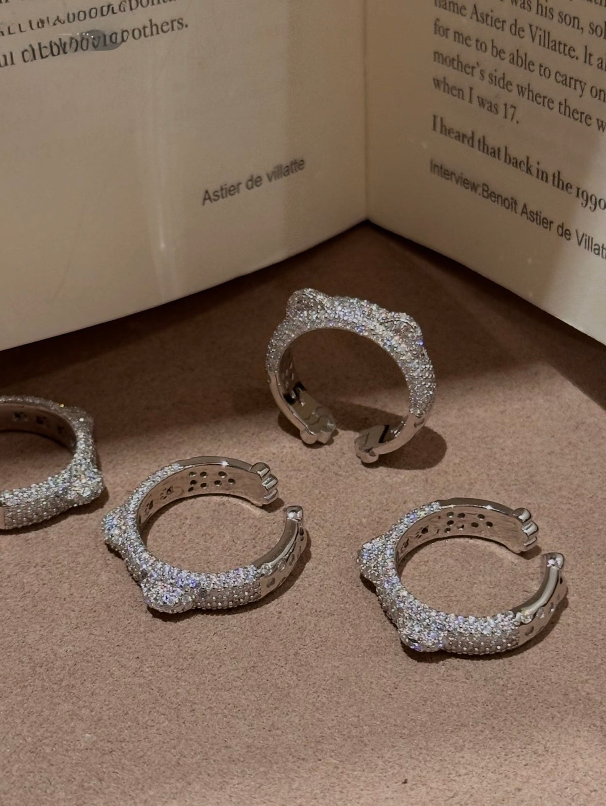 Four silver-toned huggie rings covered in clear pavé stones, arranged on a textured brown surface with an open book in the background.