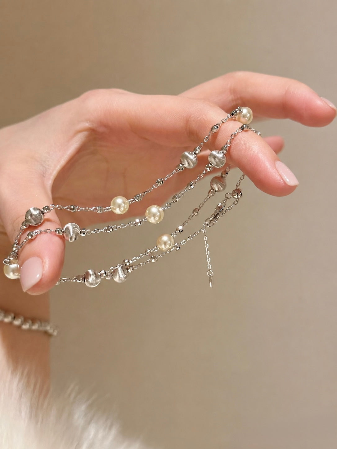 Hand wearing multiple pearl and silver chain bracelets on a neutral background