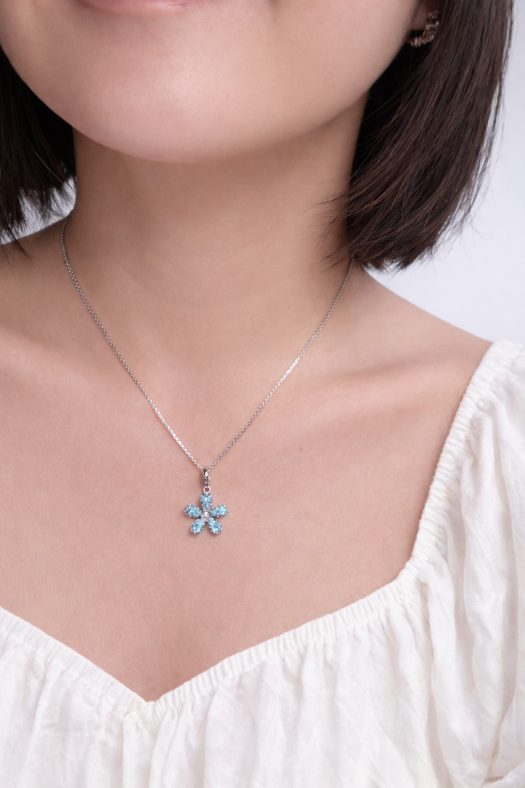 Woman wearing a necklace with a blue flower pendant against a white background