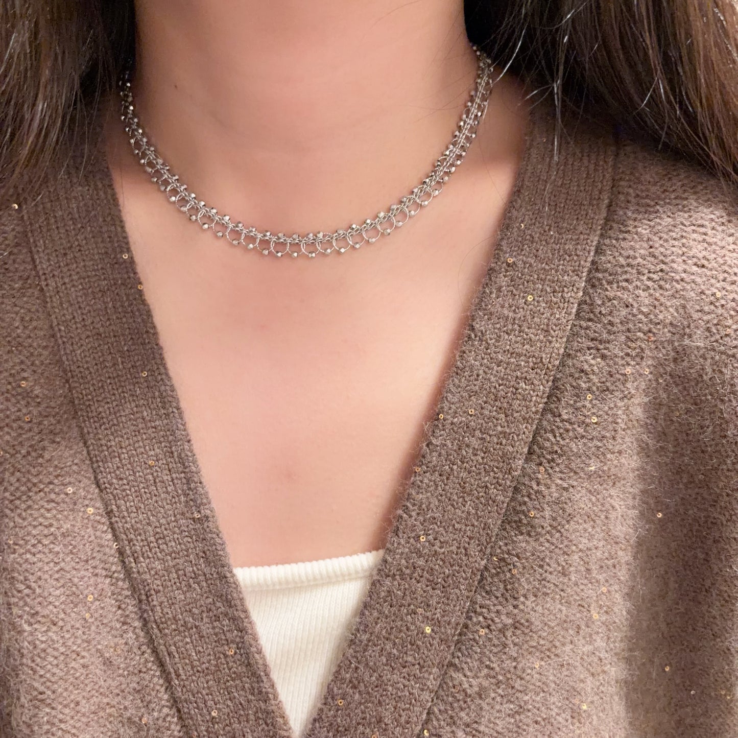 Close-up of a person wearing a silver chain necklace with a brown cardigan.
