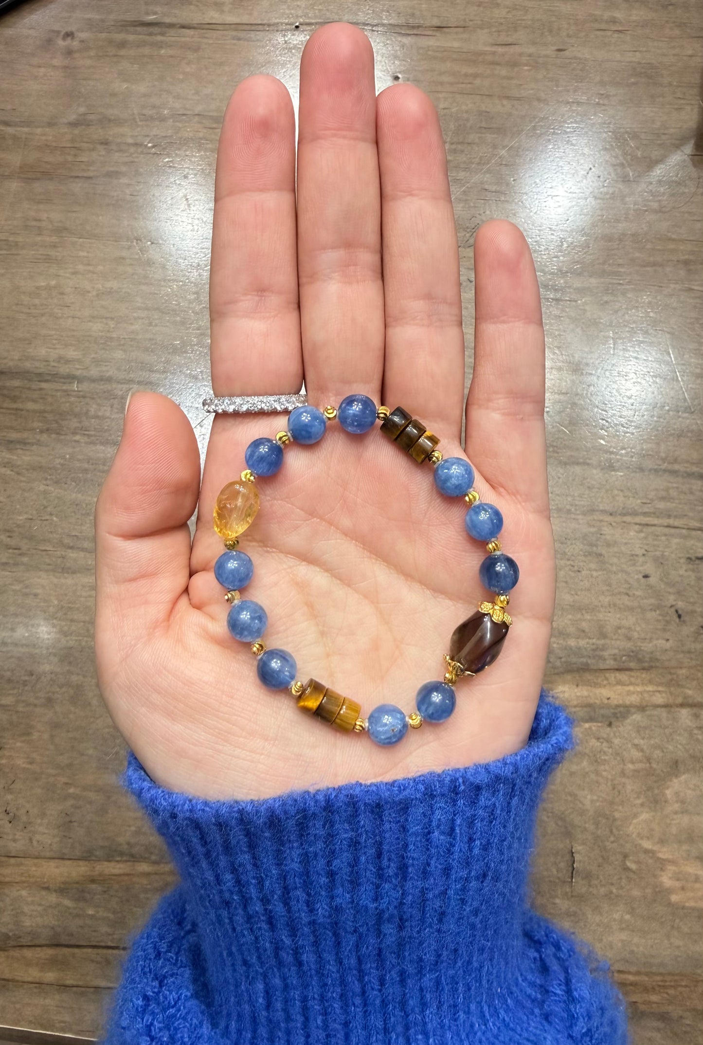 Hand holding a blue beaded bracelet on a wooden surface