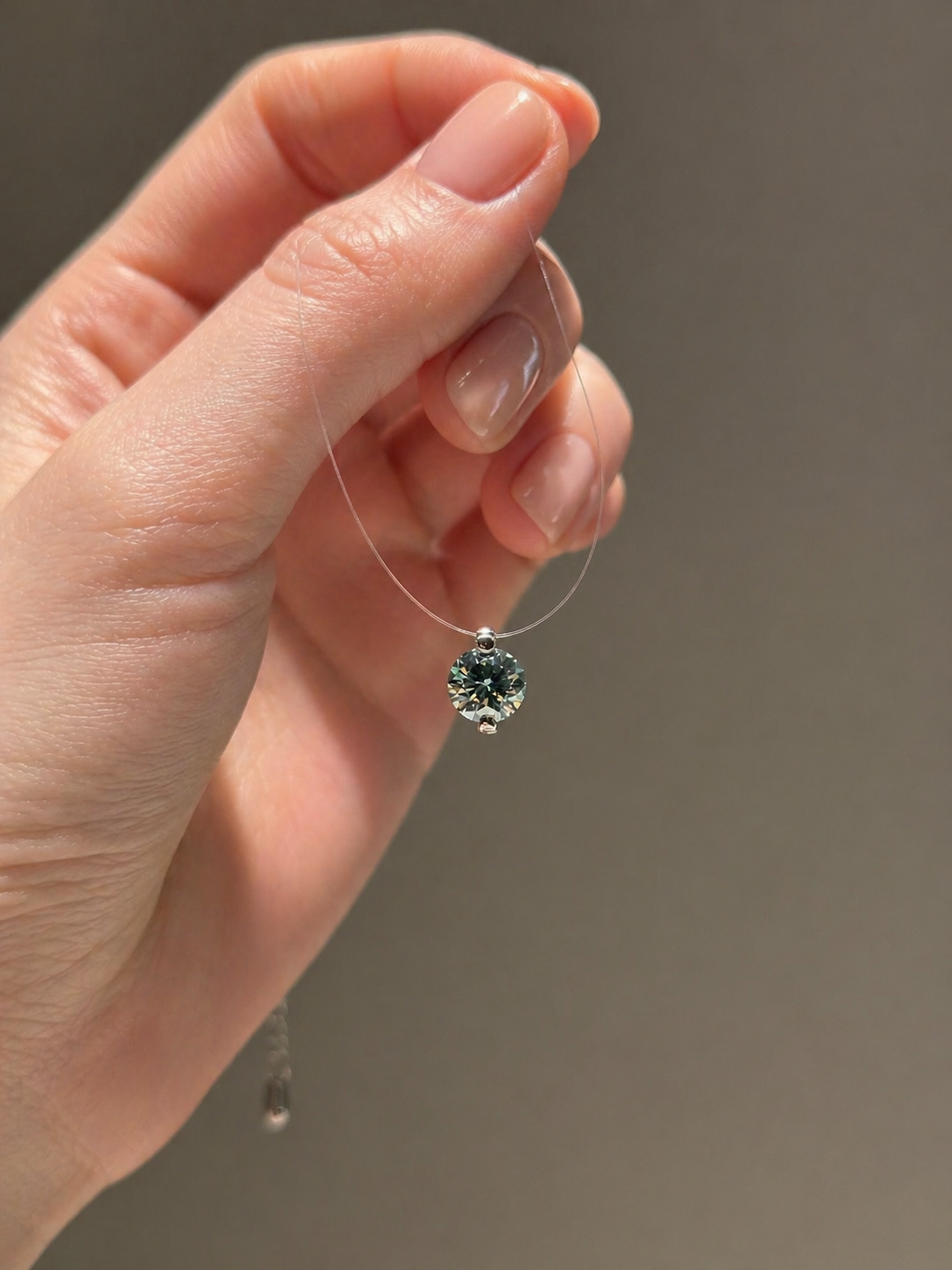 Hand holding a necklace with a green gemstone pendant against a neutral background