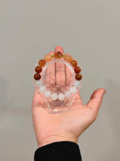 Hand holding a clear bracelet with multicolored beads against a neutral background