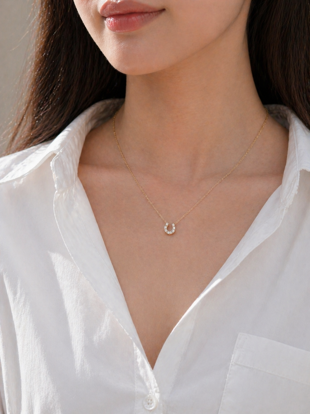 Close-up of a person wearing a delicate gold necklace with a small pendant on a plain background