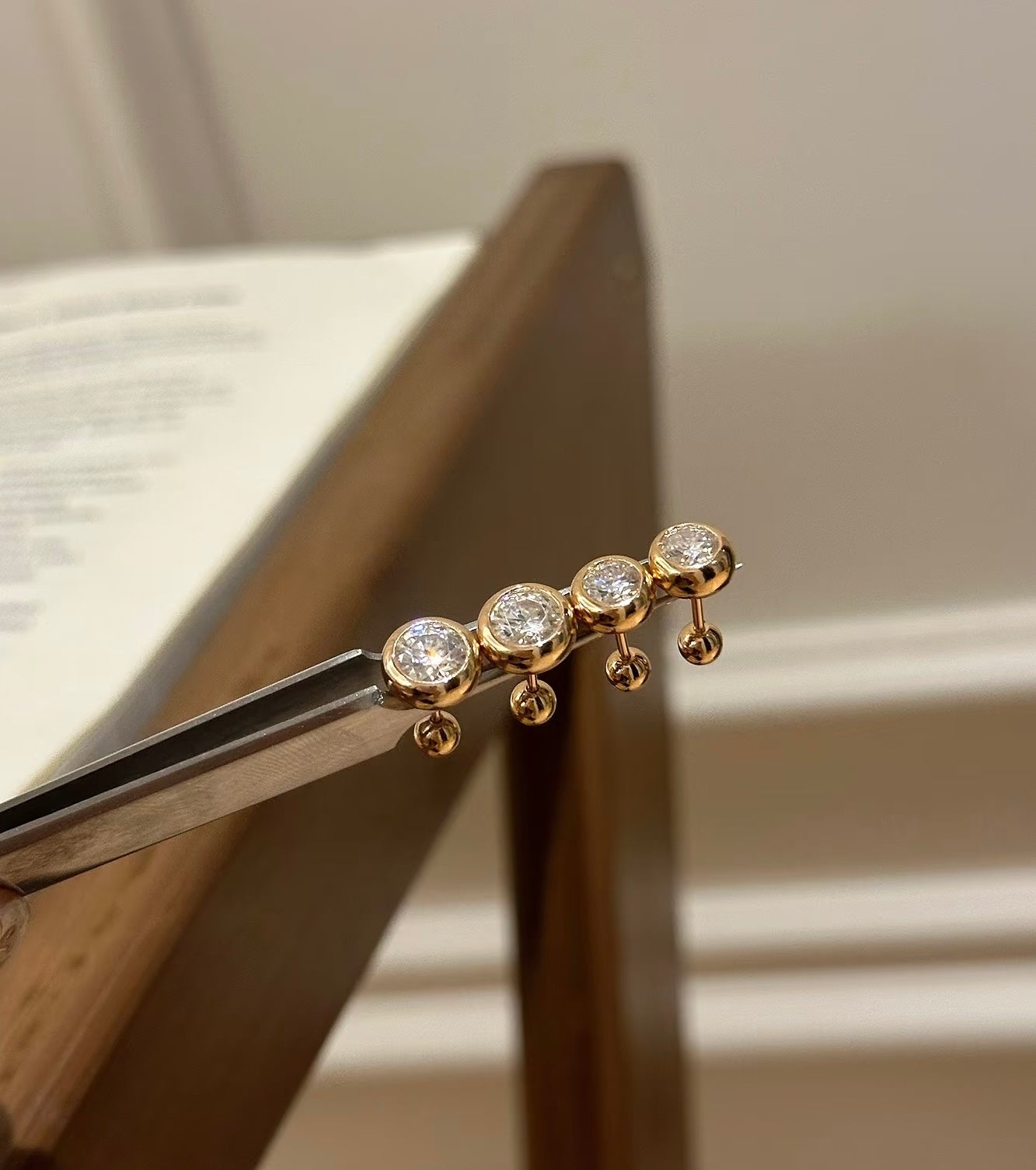 two pairs of Gold color earring with  Cubic Zirconia  held by tweezers against a neutral background