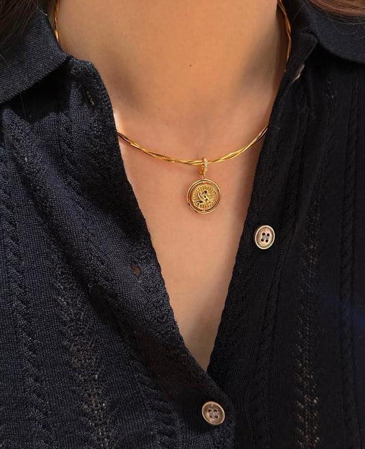 Gold necklace with a circular pendant on a person wearing a dark blue textured shirt.