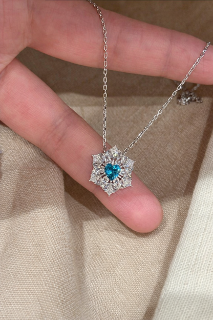 Silver necklace with a blue heart pendant held between fingers on a beige fabric background