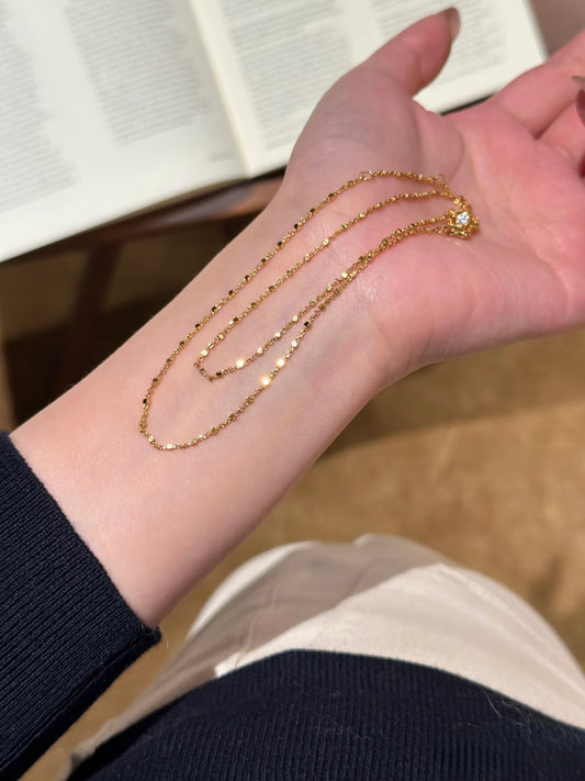 Gold chain necklace on a wrist with a neutral background