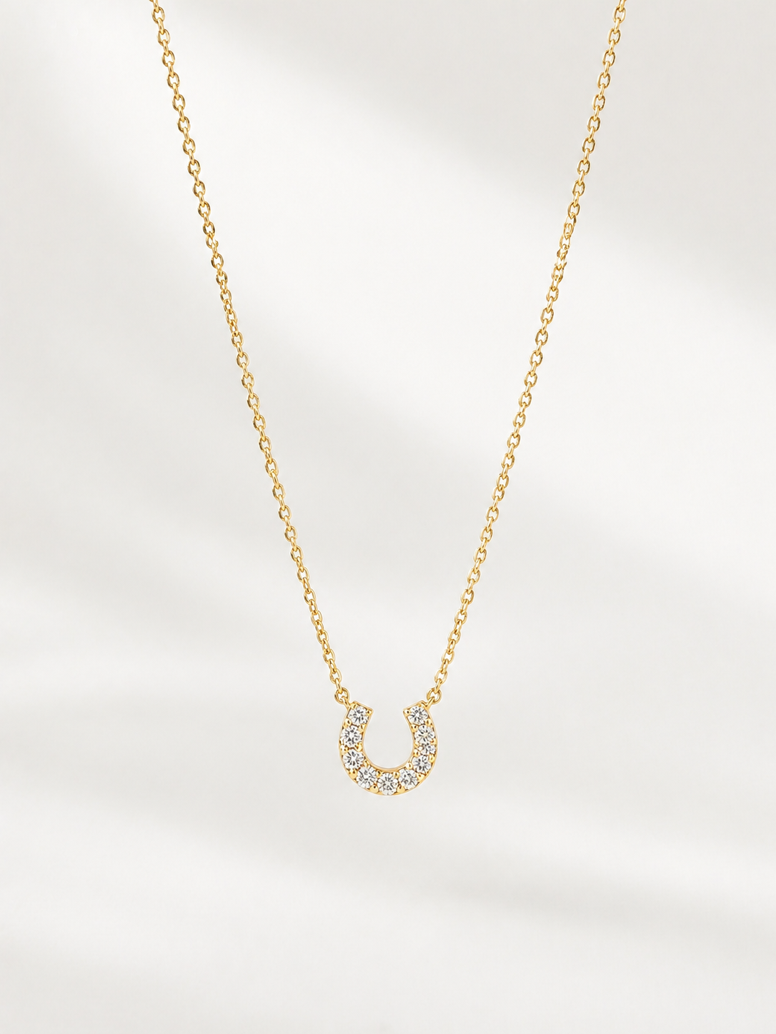 Gold necklace with a horseshoe pendant on a light gray background