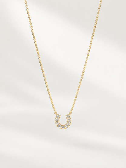 Gold necklace with a horseshoe pendant on a light gray background