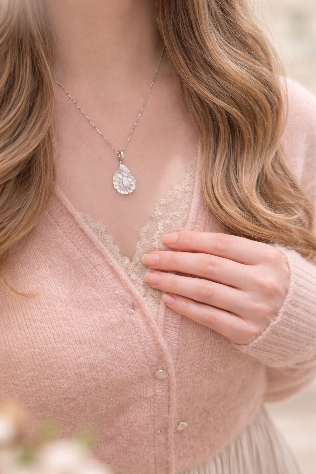 Person wearing a pink cardigan and delicate necklace with a blurred background