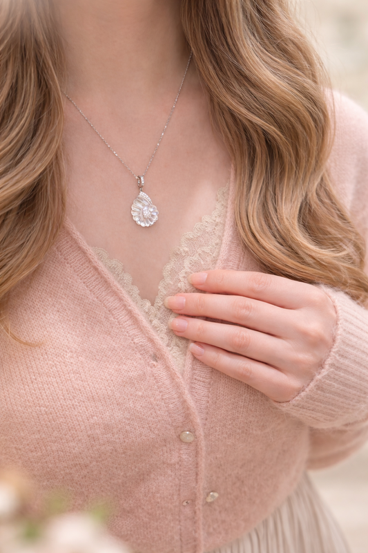 Person wearing a pink cardigan and delicate necklace with a blurred background