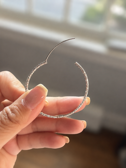 Hand holding a silver hoop earring with a blurred background