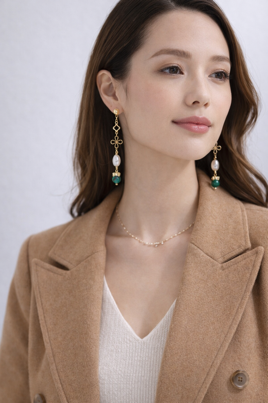 Woman wearing a beige coat with pearl earrings and a necklace against a white background