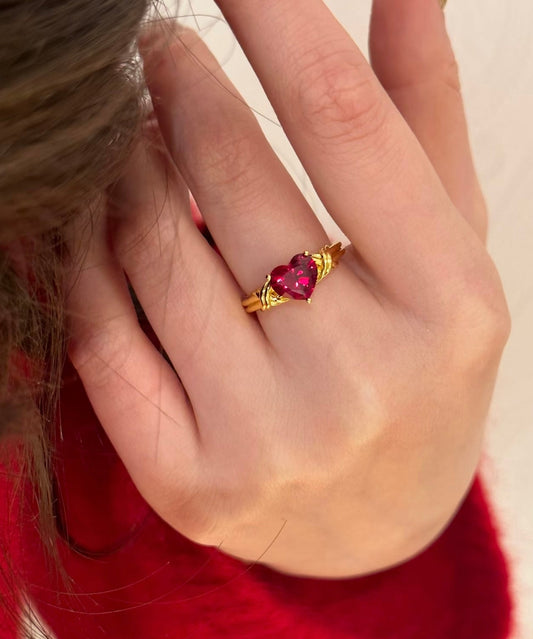 Gold ring with a red gemstone on a hand against a neutral background