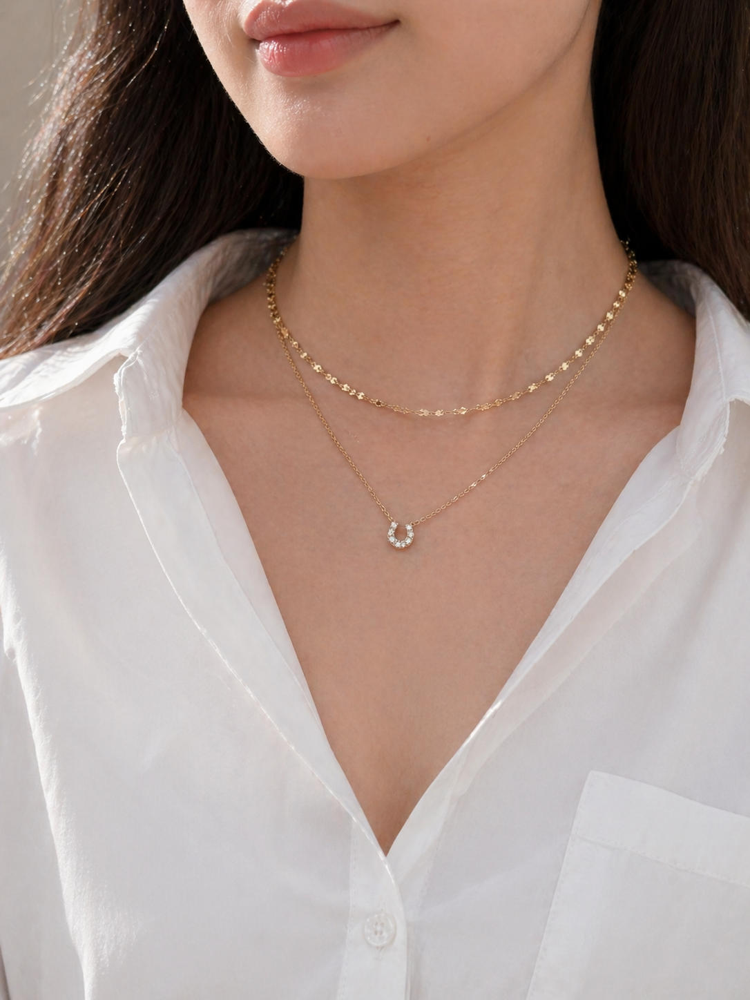 Close-up of a person wearing a delicate gold necklace with a small pendant against a white shirt background.