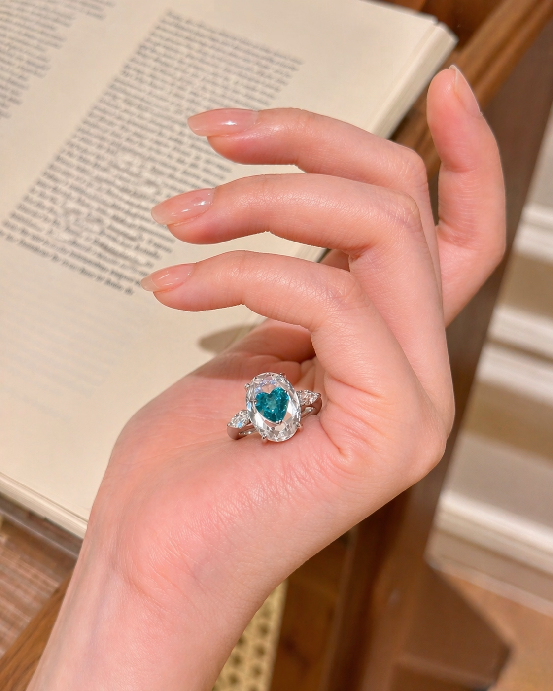Hand wearing a ring with a heart-shaped gemstone on a blurred background