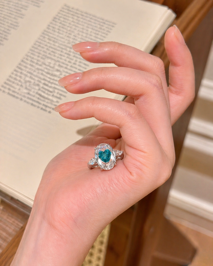 Hand wearing a ring with a heart-shaped gemstone on a blurred background