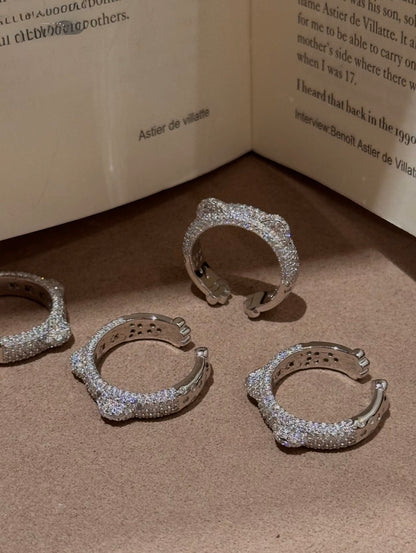 Four silver-toned huggie rings covered in clear pavé stones, arranged on a textured brown surface with an open book in the background.