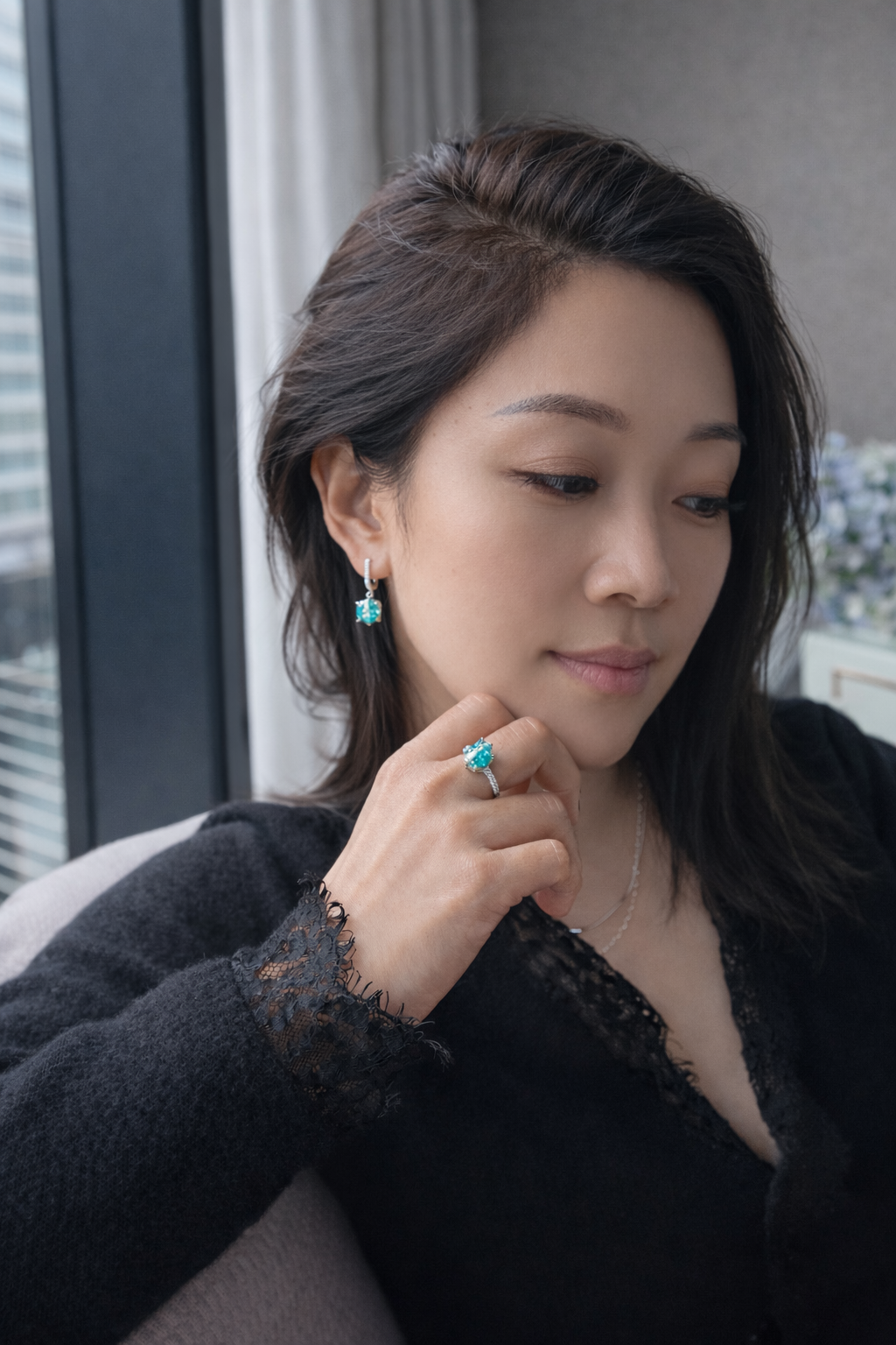 Woman wearing earrings and a black top, looking down.
