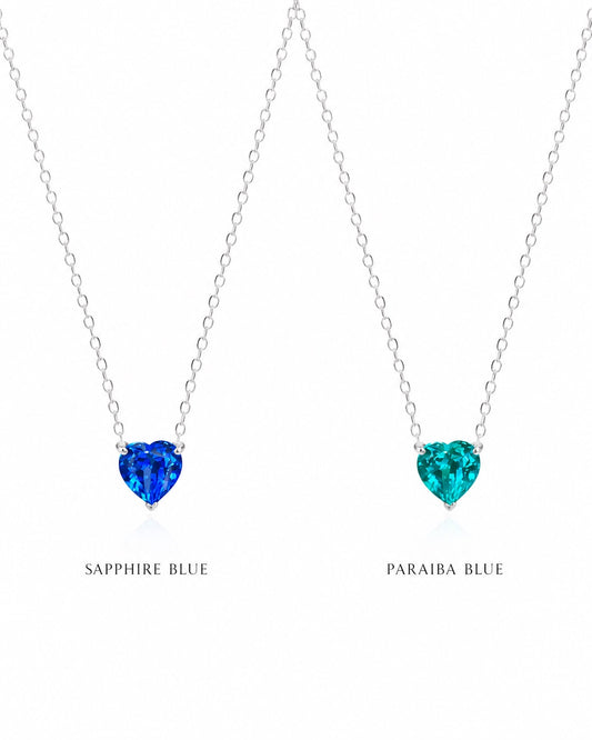 Two heart-shaped gemstone necklaces, one sapphire blue and one paraiba blue, on a white background.