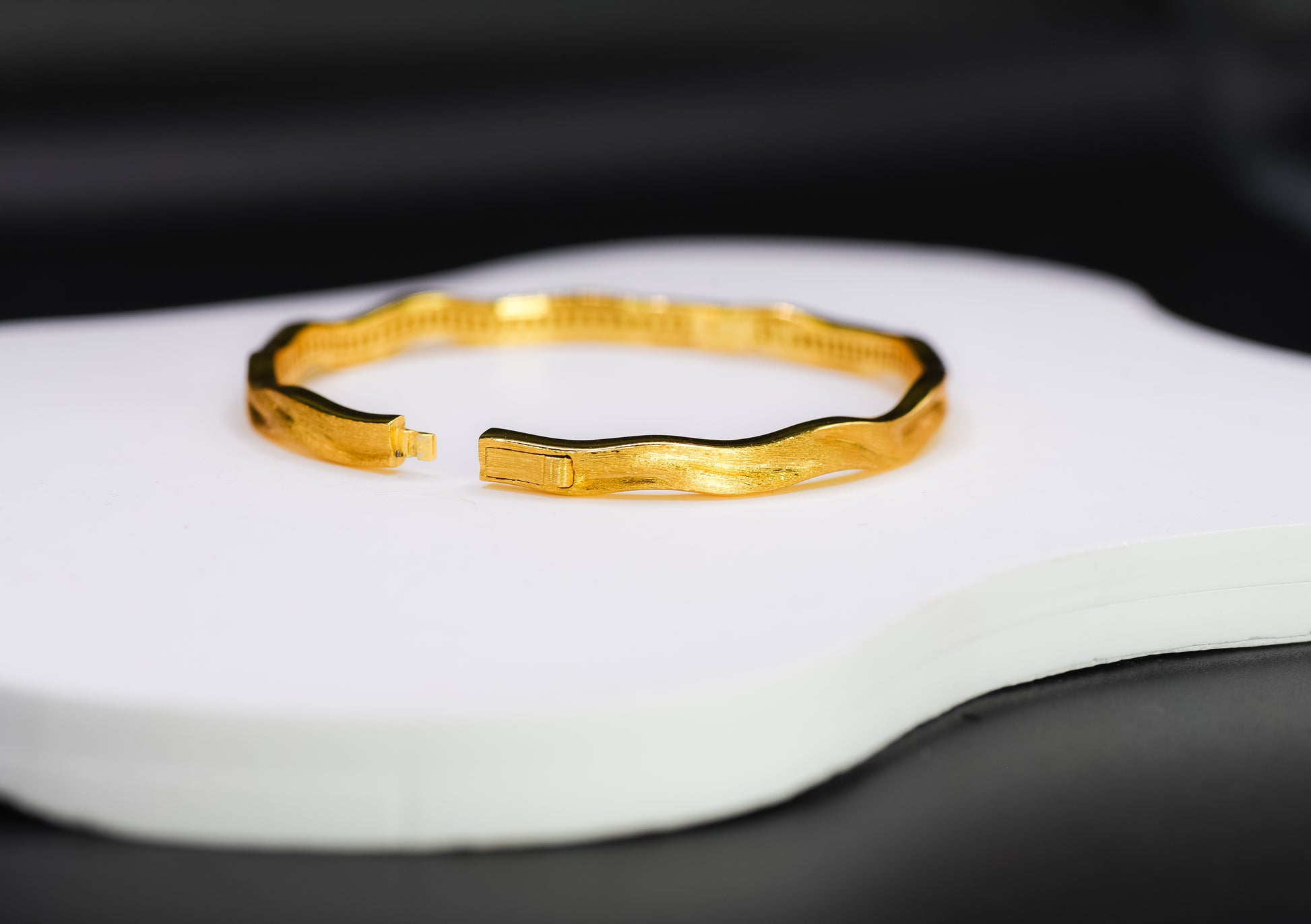 Gold color bracelet on a white surface with a black background