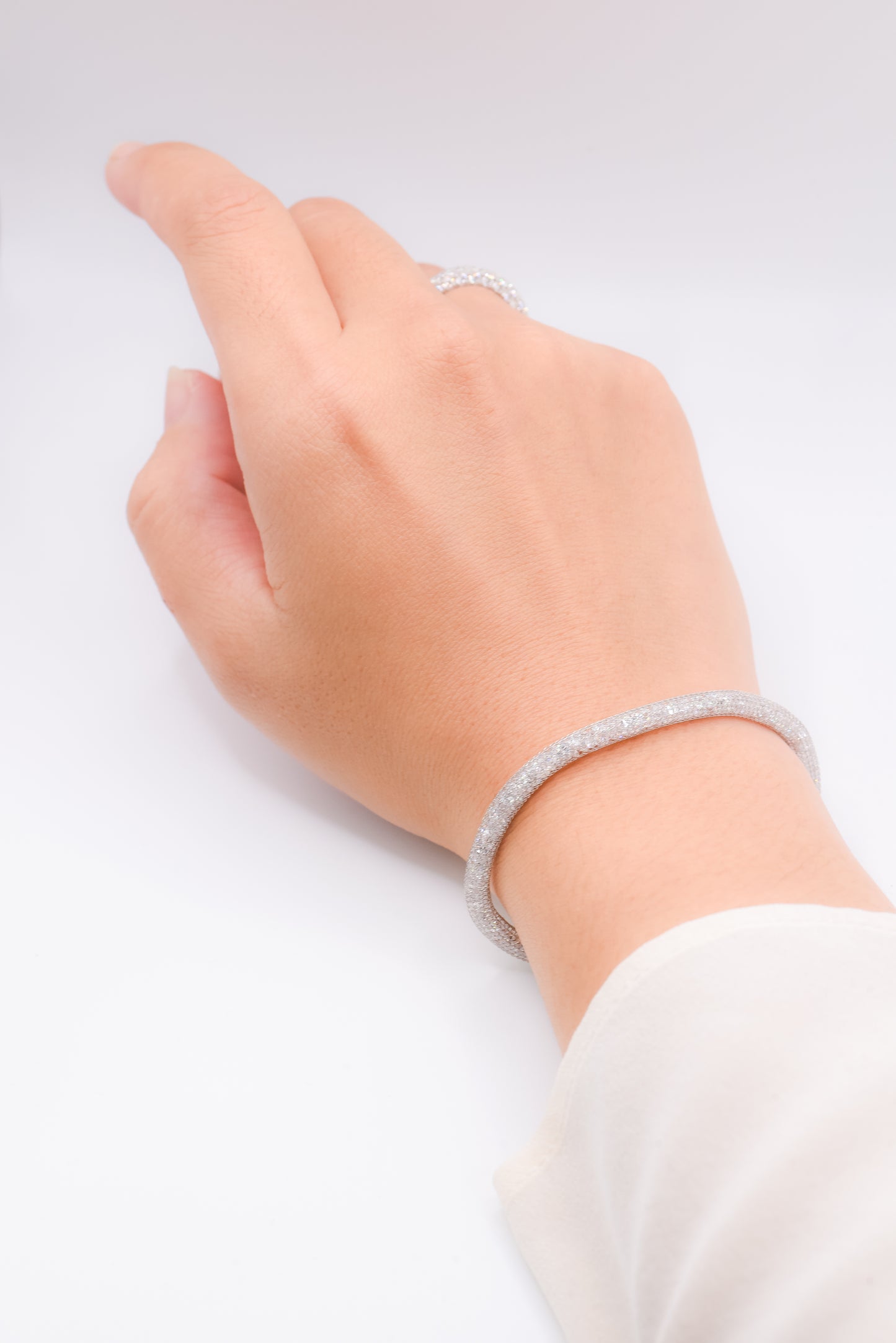 Hand wearing a silver bracelet on a light gray background