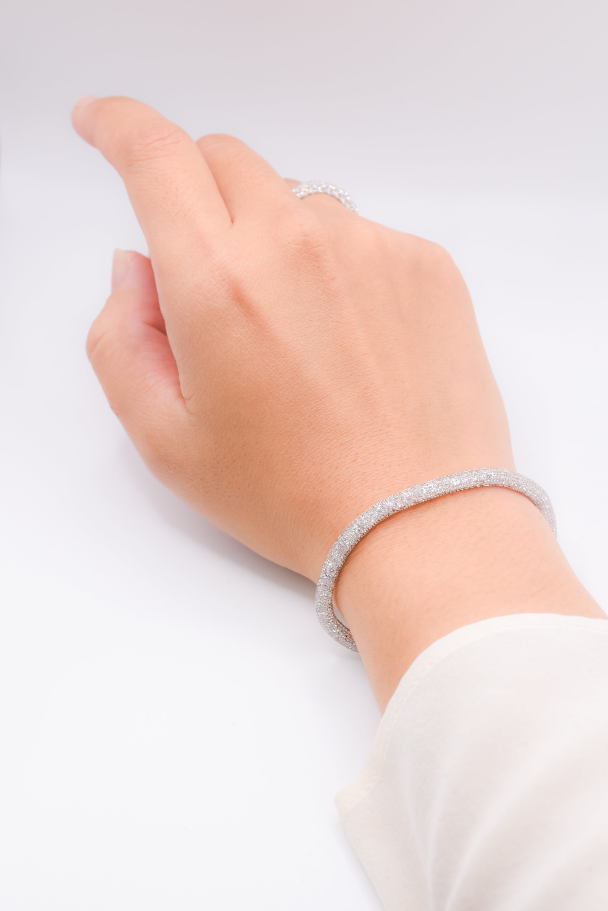 Hand wearing a silver bracelet on a light gray background