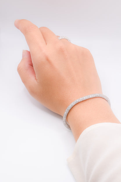 Hand wearing a silver bracelet on a light gray background