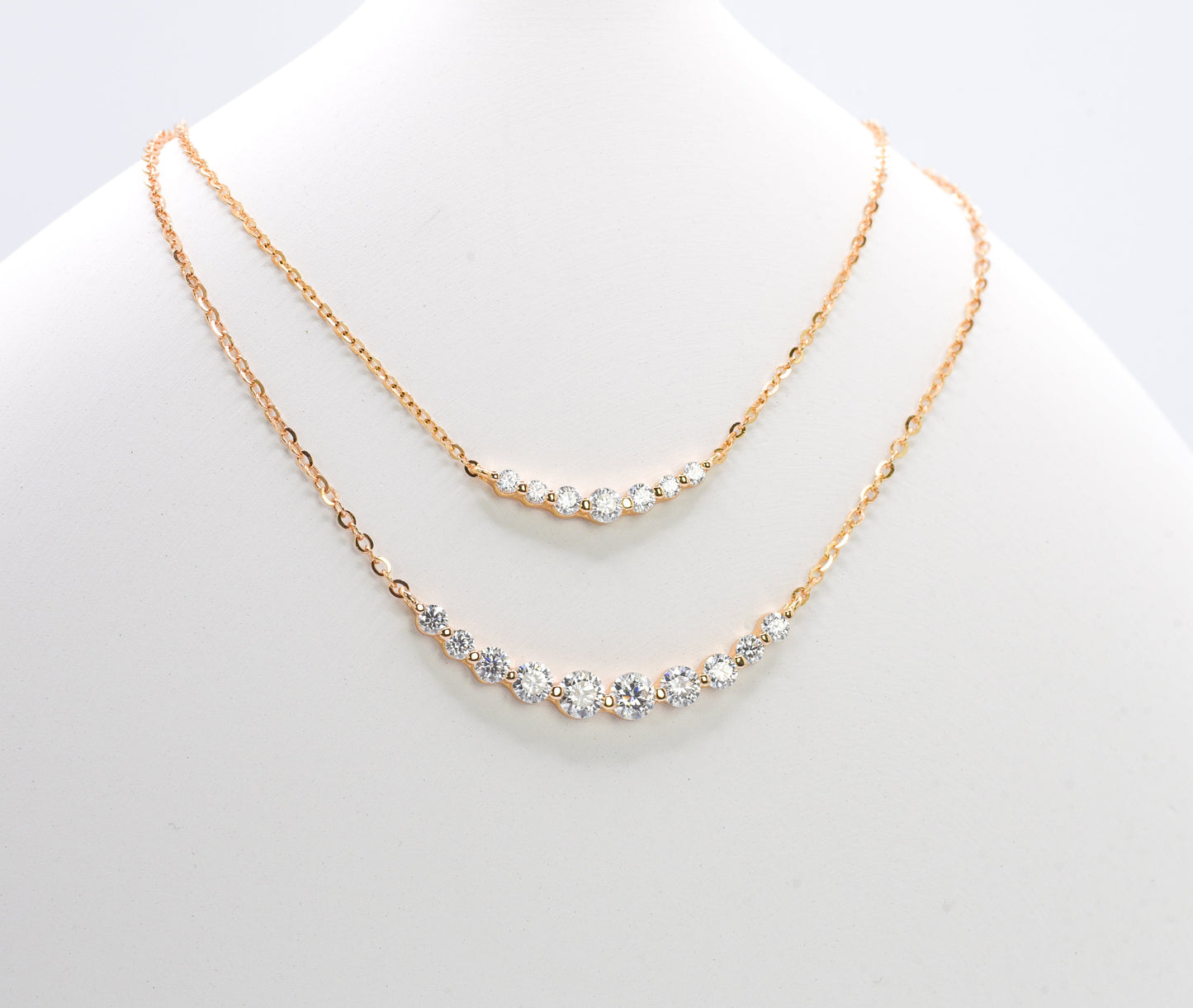 Two gold color of necklaces with gemstones on a white mannequin.