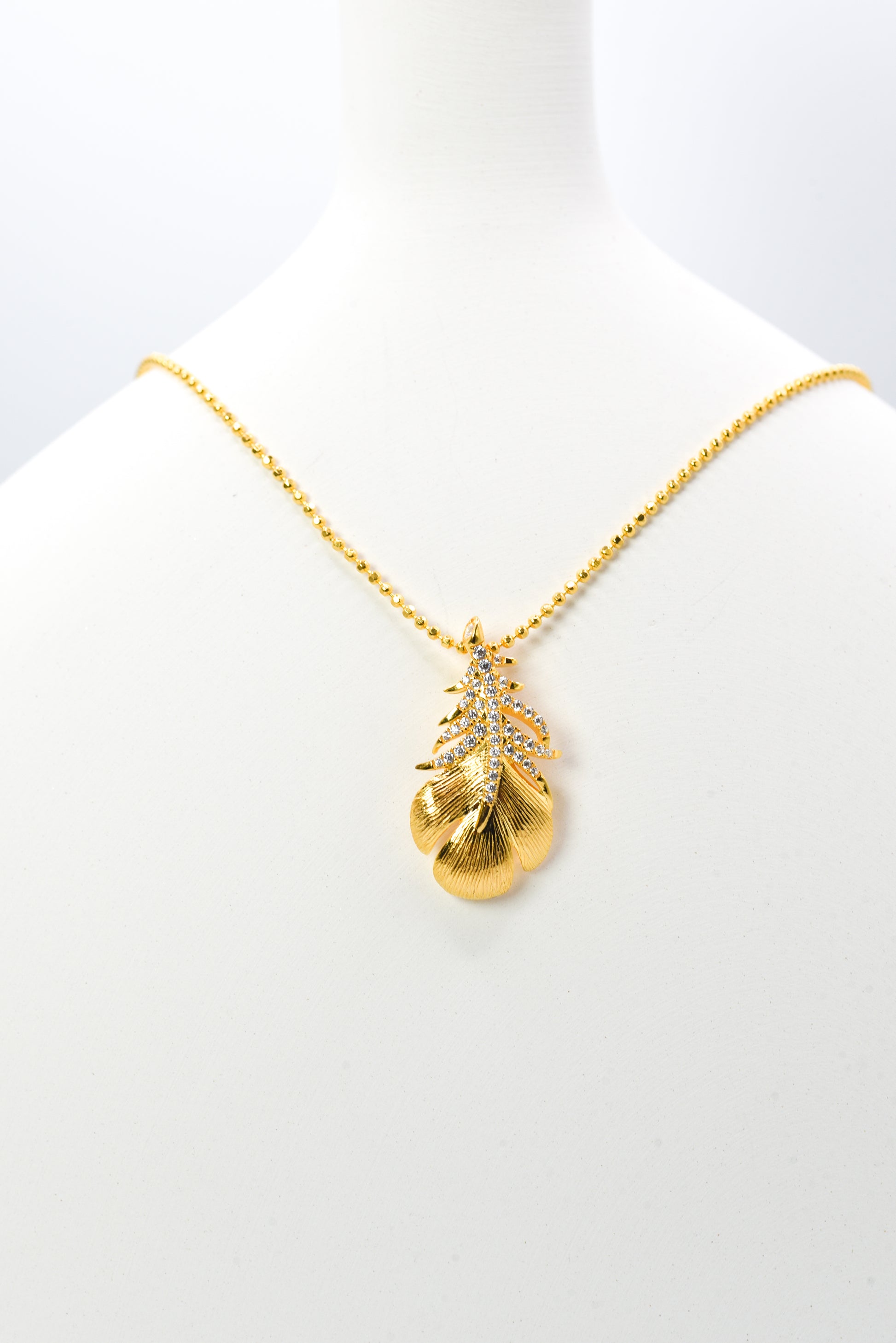 Gold color necklace with a leaf-shaped pendant on a white background