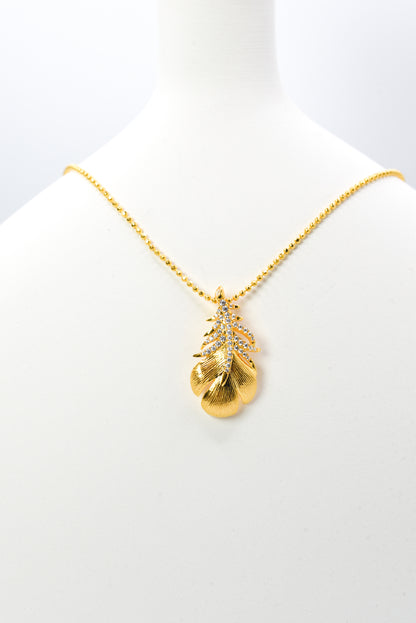 Gold color necklace with a leaf-shaped pendant on a white background