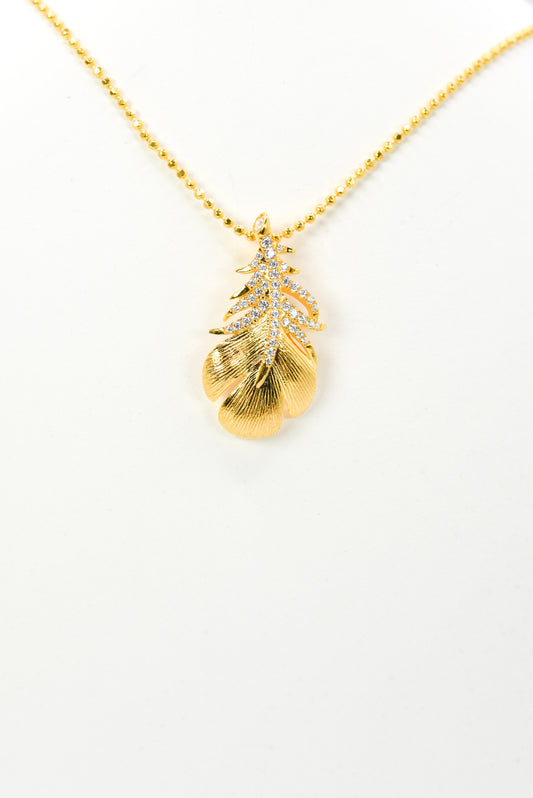 Gold color necklace with a leaf-shaped pendant on a white background