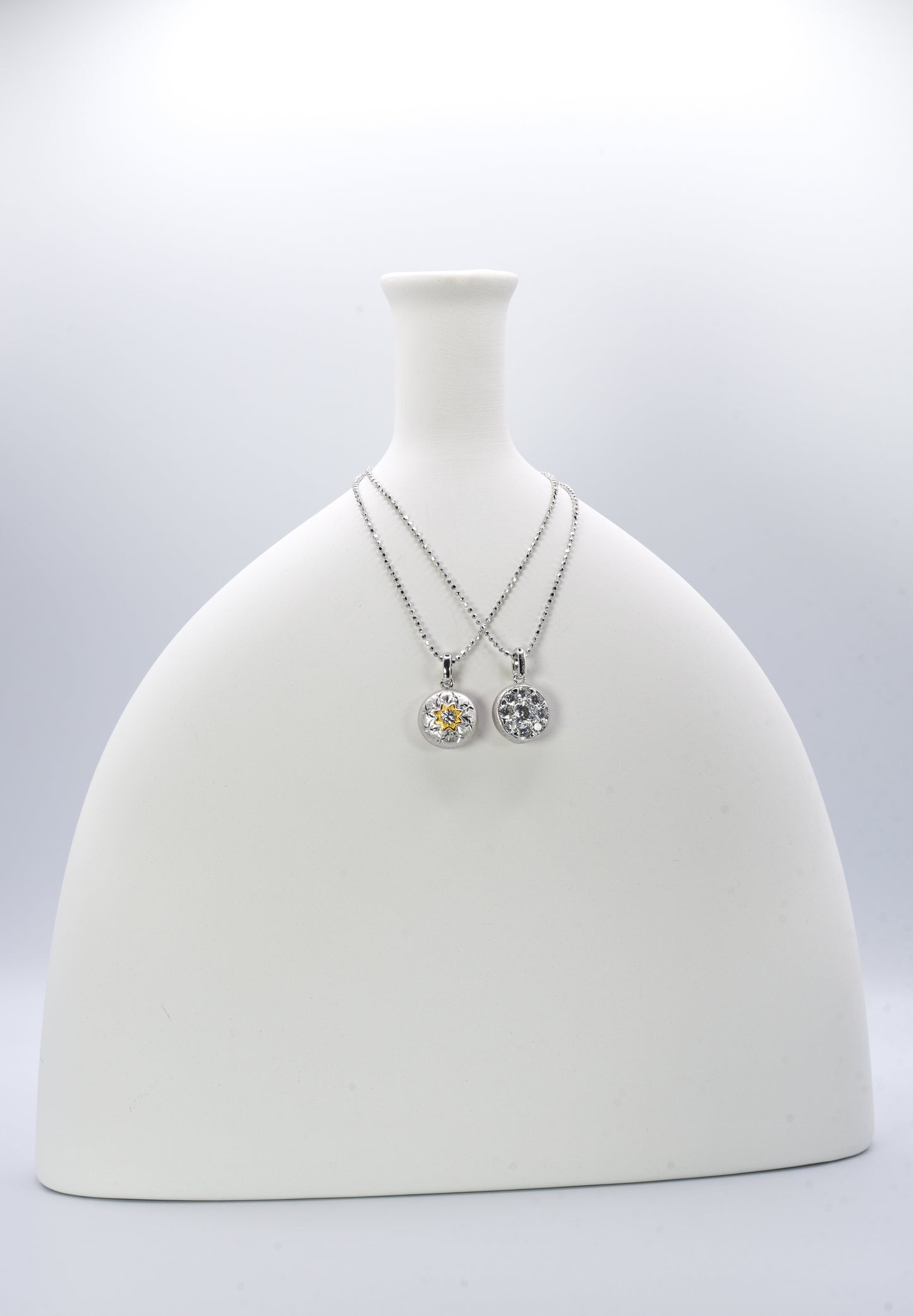 Two silver necklaces with round pendants on a white mannequin bust against a light gray background