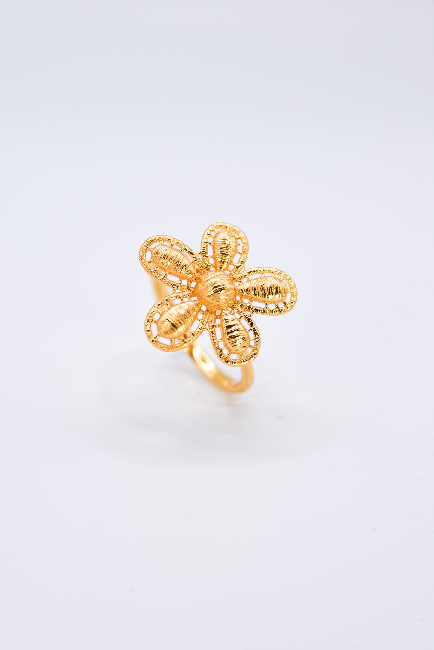 Gold flower-shaped ring on a light gray background