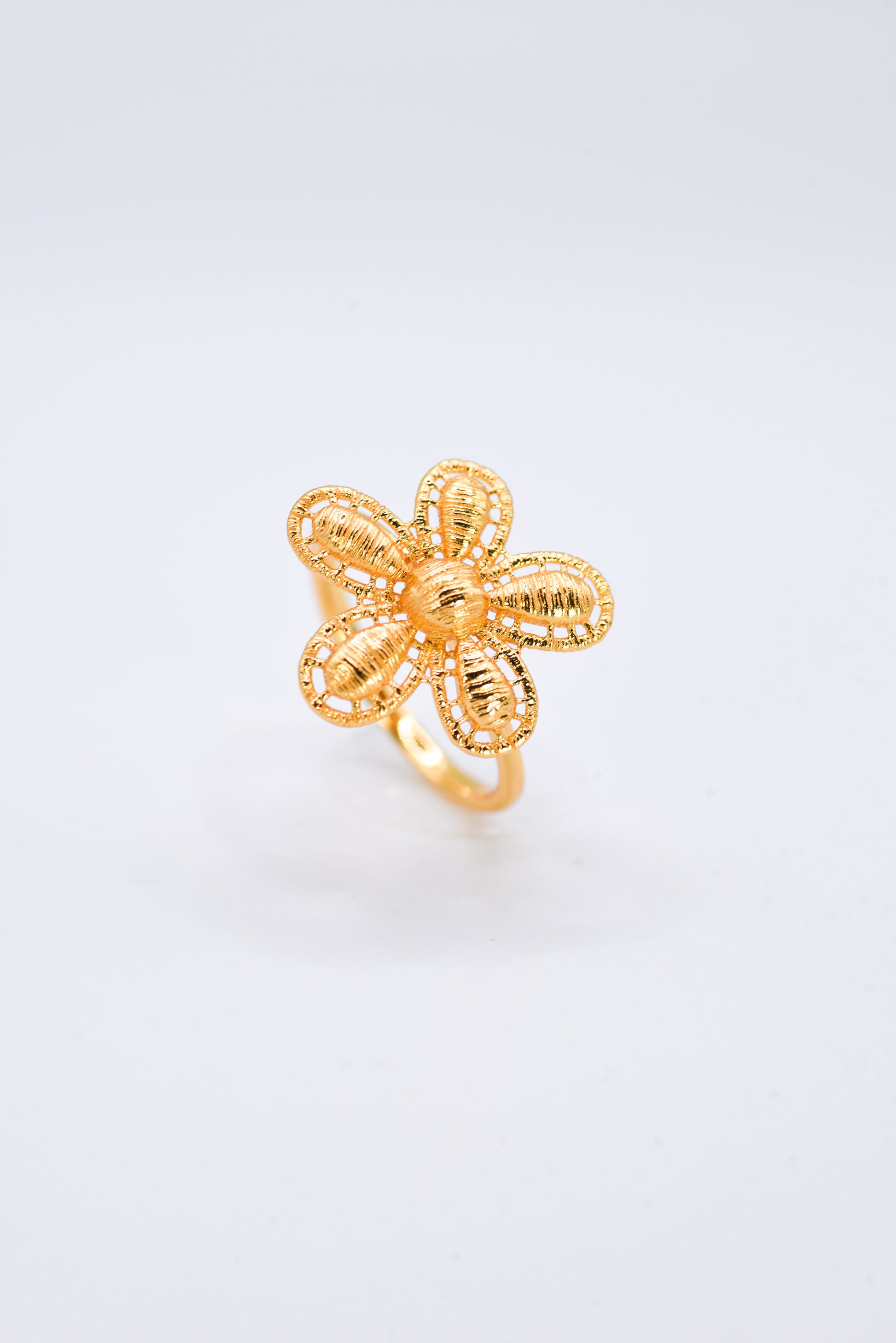 Gold flower-shaped ring on a light gray background