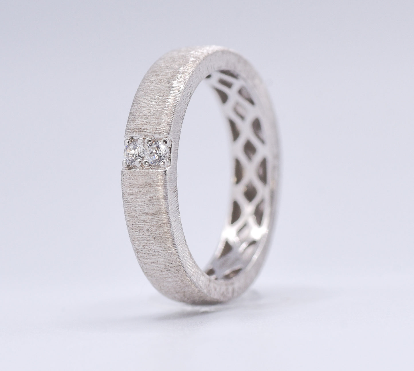 Silver ring with lattice design and embedded gemstones on a light gray background