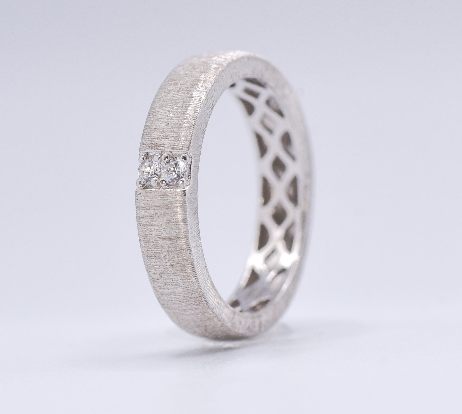 Silver ring with lattice design and embedded gemstones on a light gray background