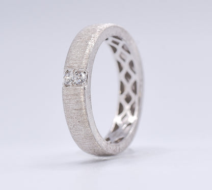 Silver ring with lattice design and embedded gemstones on a light gray background