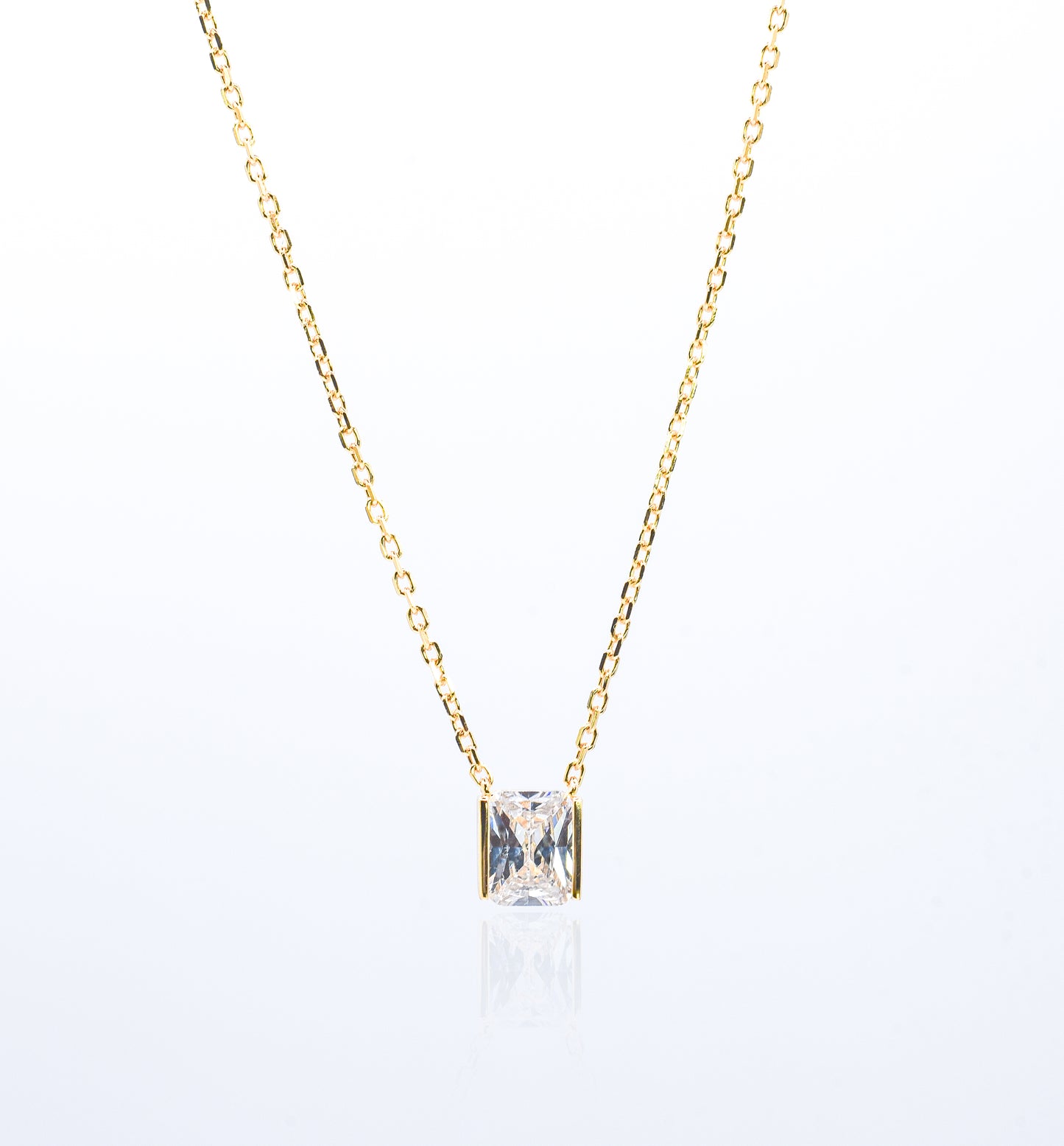 Gold color necklace with a square-cut gemstone pendant on a white background