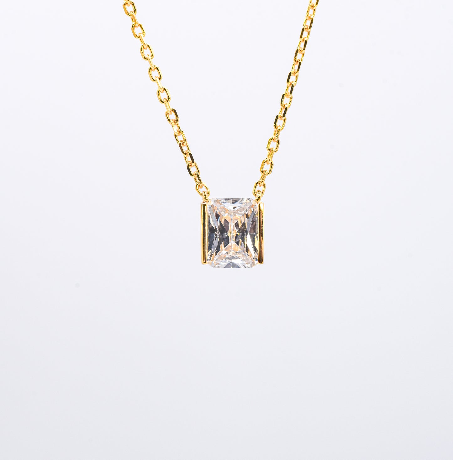 Gold color necklace with a square-cut gemstone pendant on a light gray background