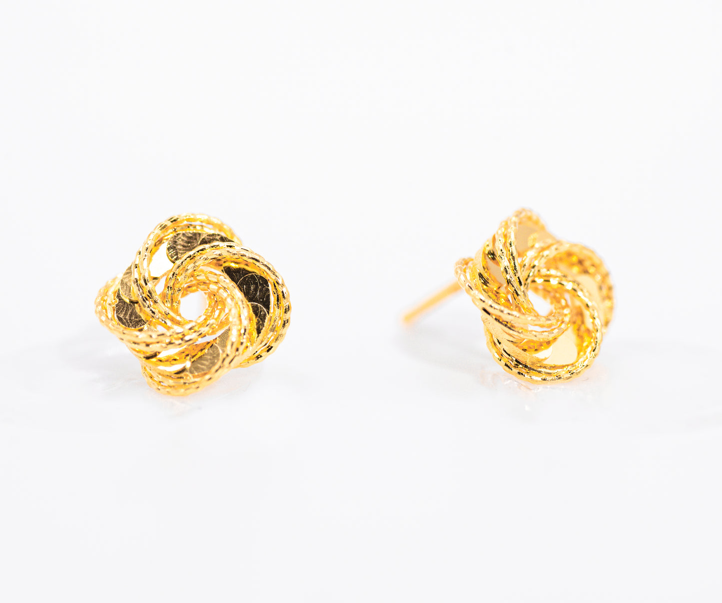 Pair of gold color knot earrings on a white background