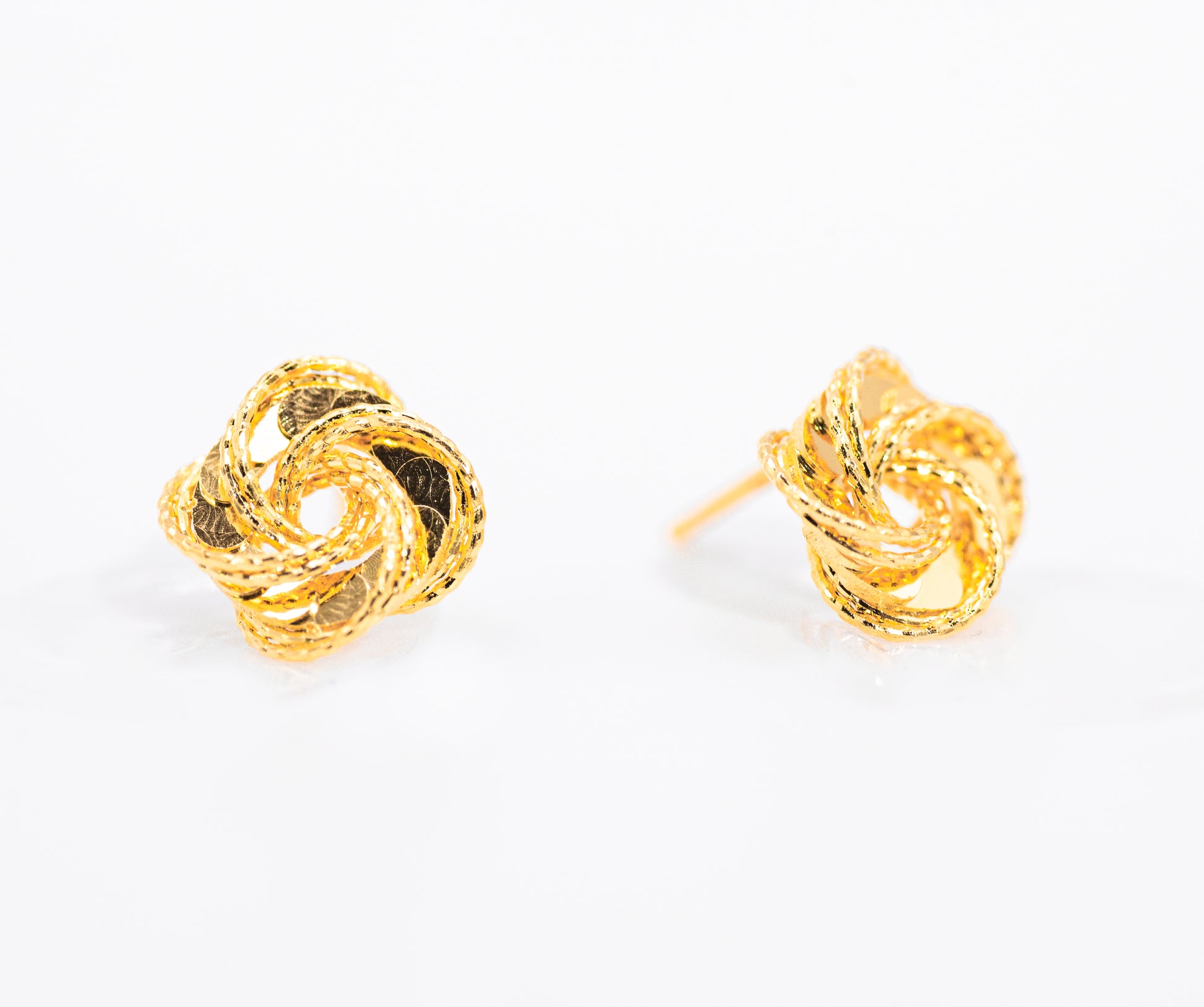 Pair of gold color knot earrings on a white background