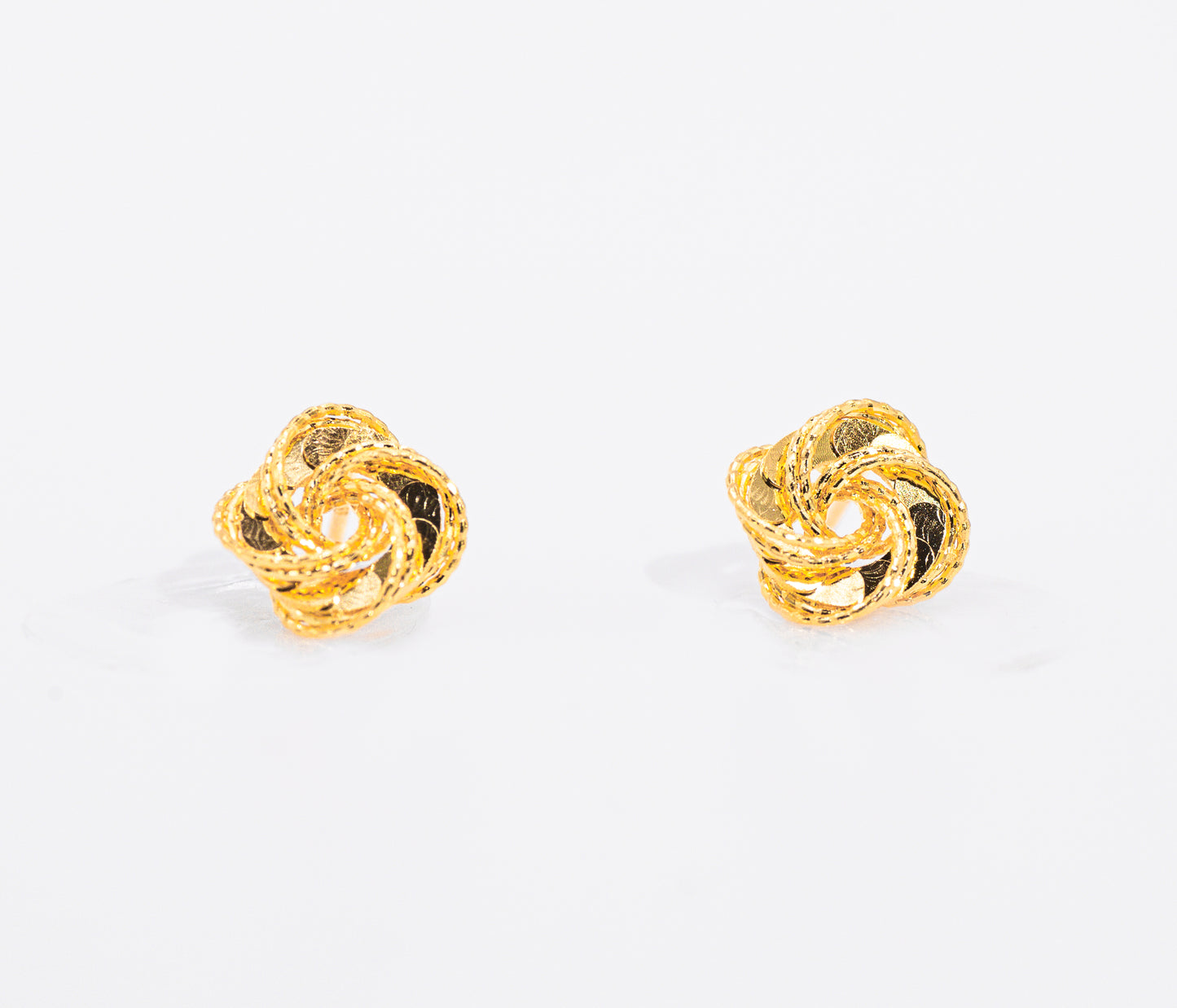 Pair of gold color knot earrings on a white background