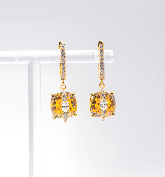 Gold color earrings with yellow gemstones on a white background