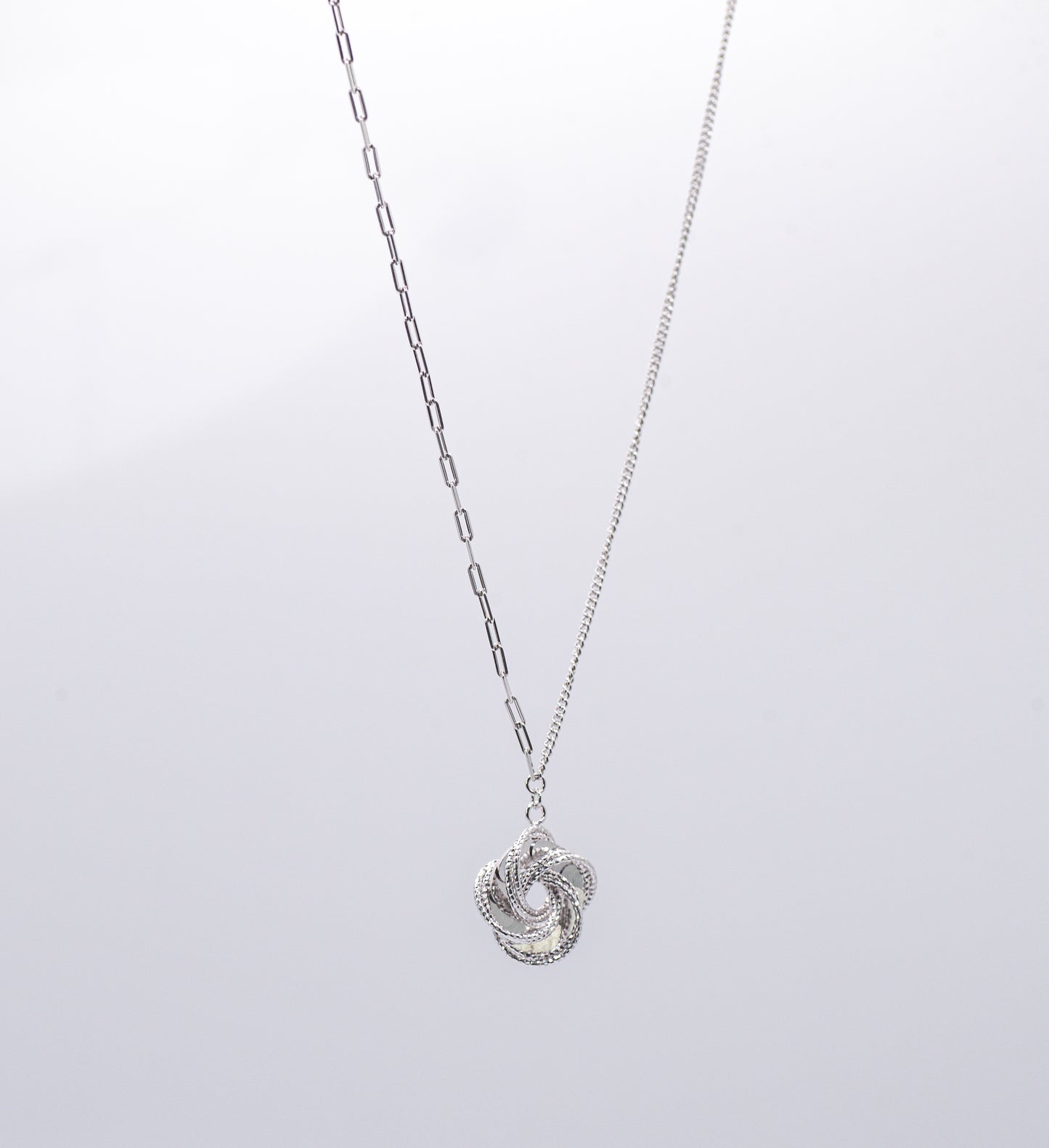 Silver necklace with a  intricate pendant on a light gray background