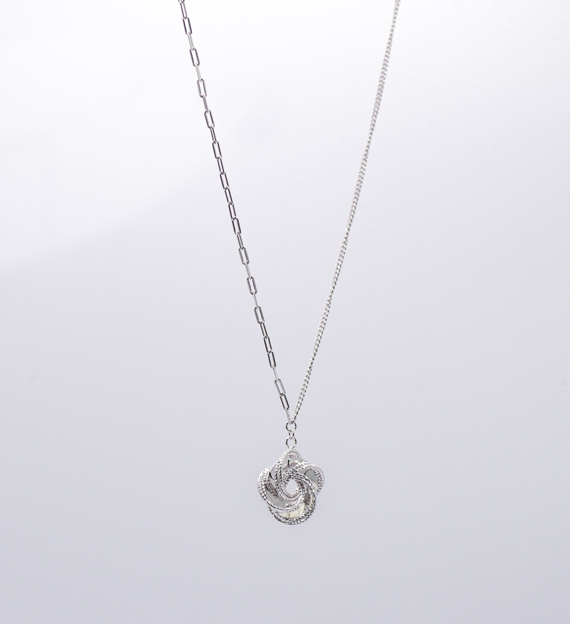 Silver necklace with a  intricate pendant on a light gray background