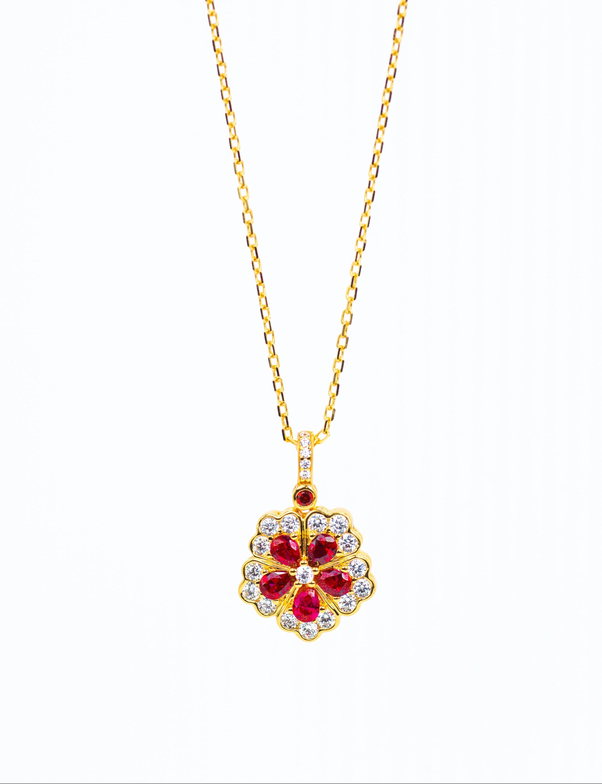 Gold necklace with a red gemstone pendant on a white background